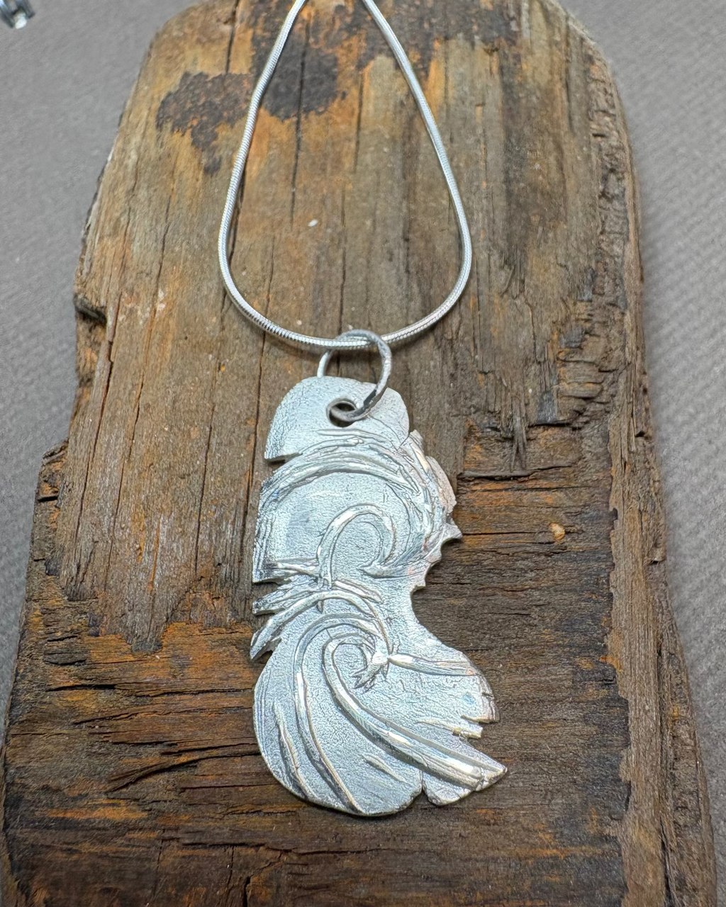 Silver surf pendant with silver cord chain on a piece of driftwood