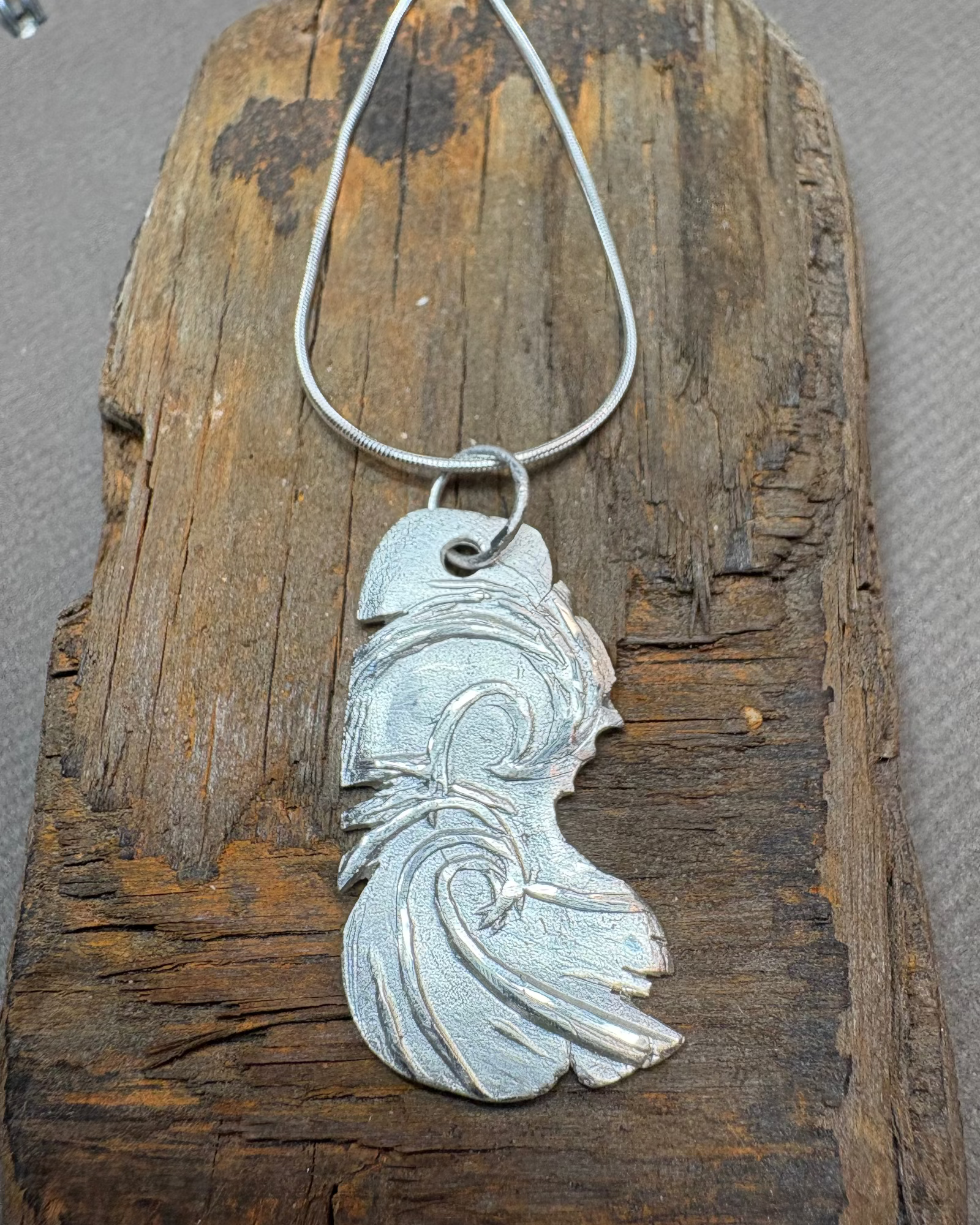 Silver surf pendant with silver cord chain on a piece of driftwood
