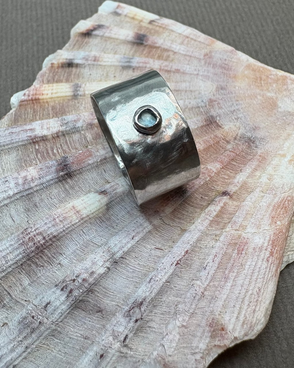 Hammered silver ring set with a topaz stone on a shell background