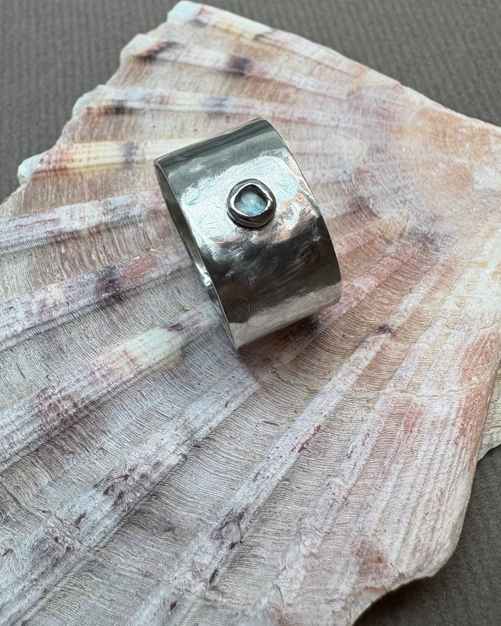 Hammered silver ring set with a topaz stone on a shell background