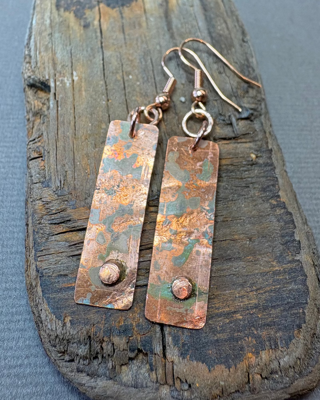 Pair of copper oxidised earrings on a textured driftwood surface