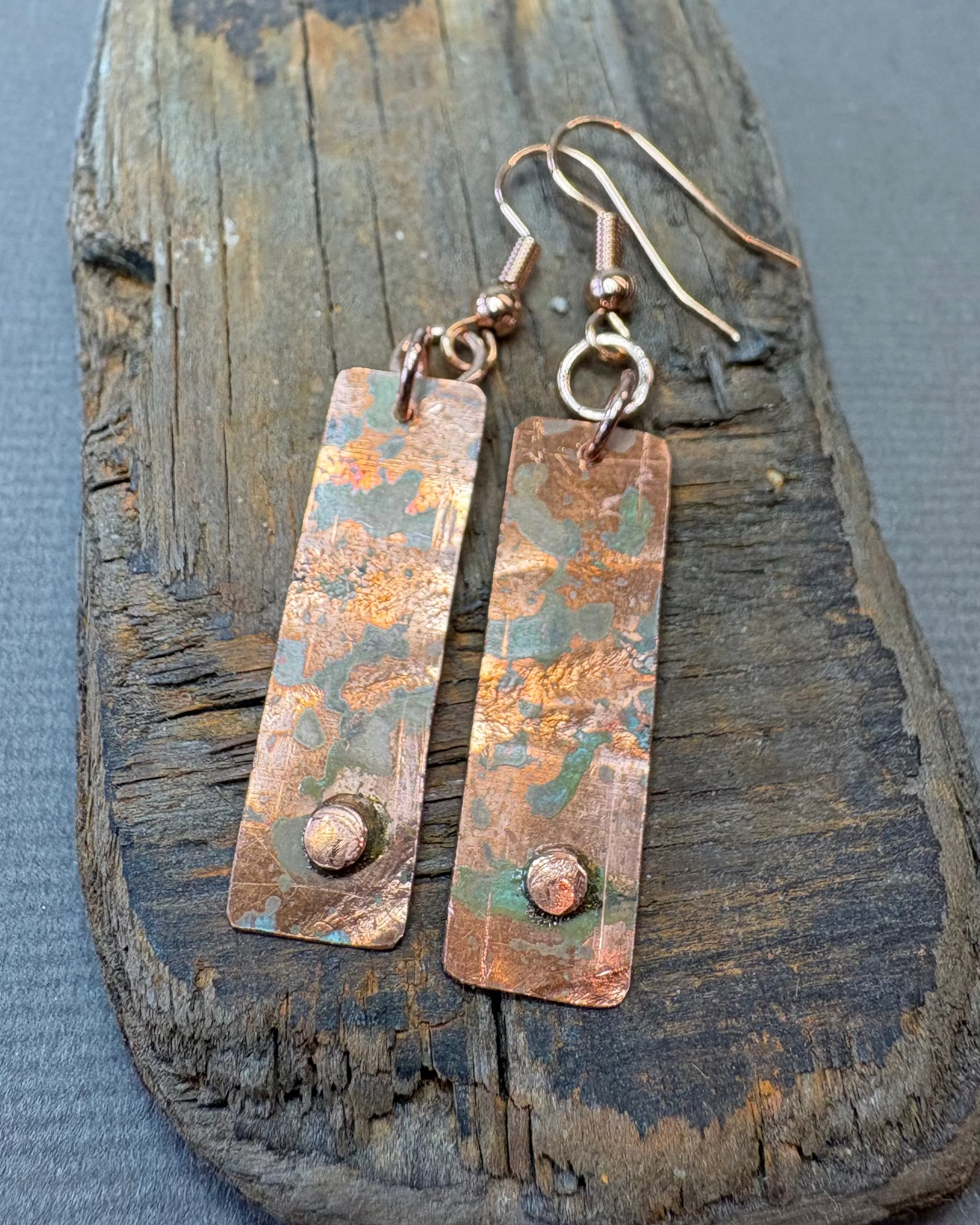 Pair of copper oxidised earrings on a textured driftwood surface