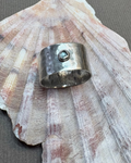 Hammered silver ring set with a topaz stone pictured on a shell