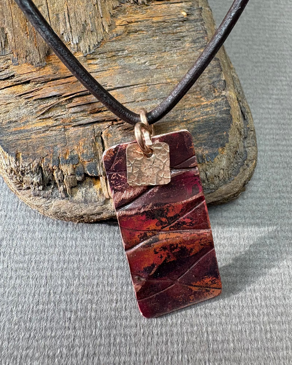 Necklace with an  oxidised rectangular pendant on a driftwood surface