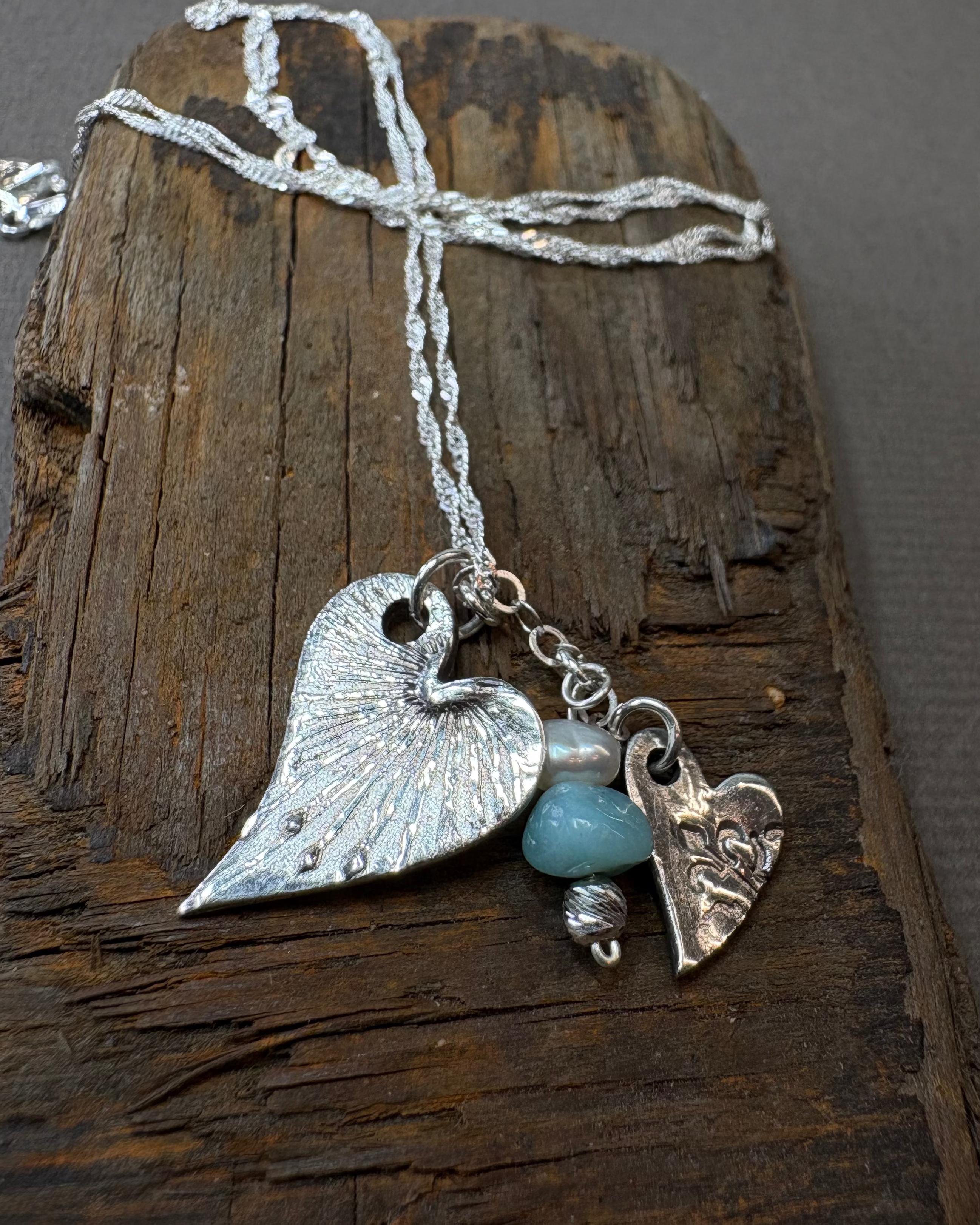 Necklace with two heart charms and a apatite bead and pearl on driftwood