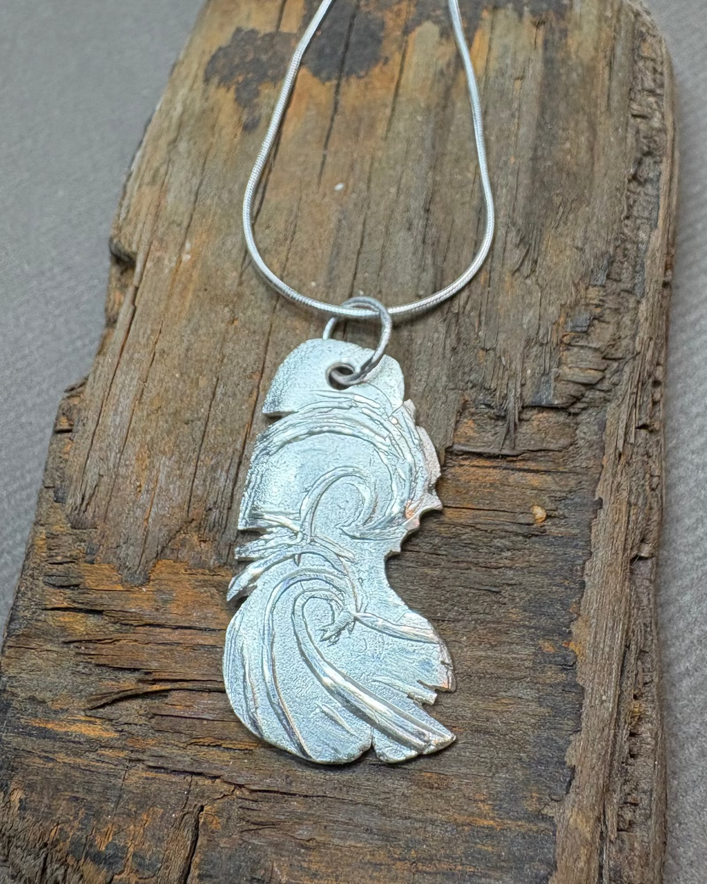 Silver surf pendant on a driftwood surface