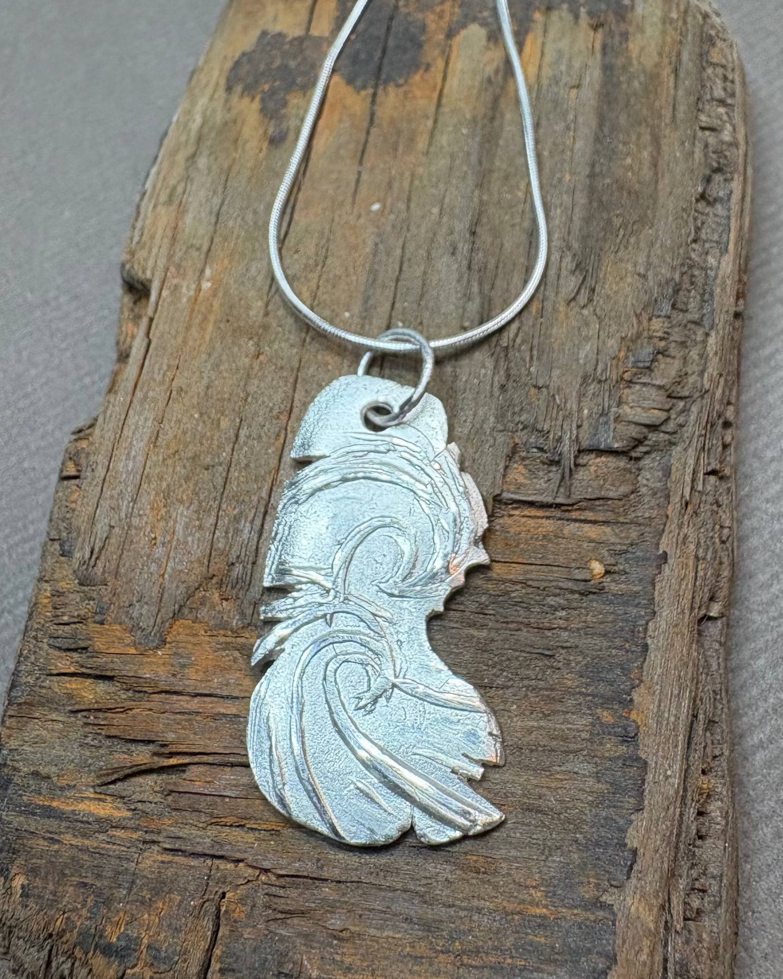 Silver surf pendant on a driftwood surface