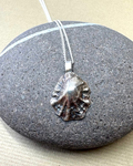 Silver limpet shell pendant on a fine silver chain over a pebble