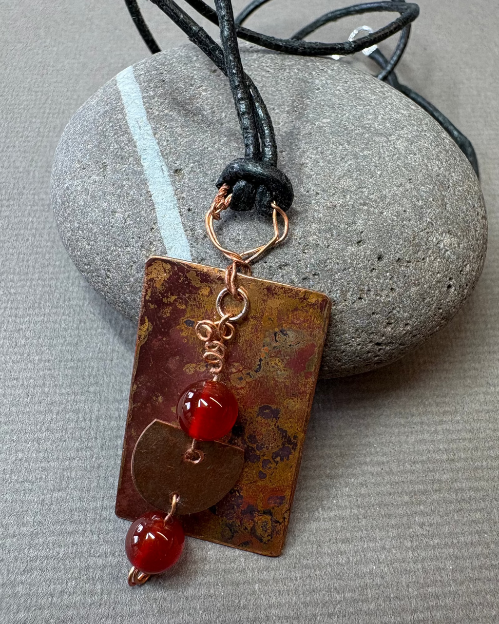 Leather with a rectangular copper oxidised pendant with carnelian beads on a pebble
