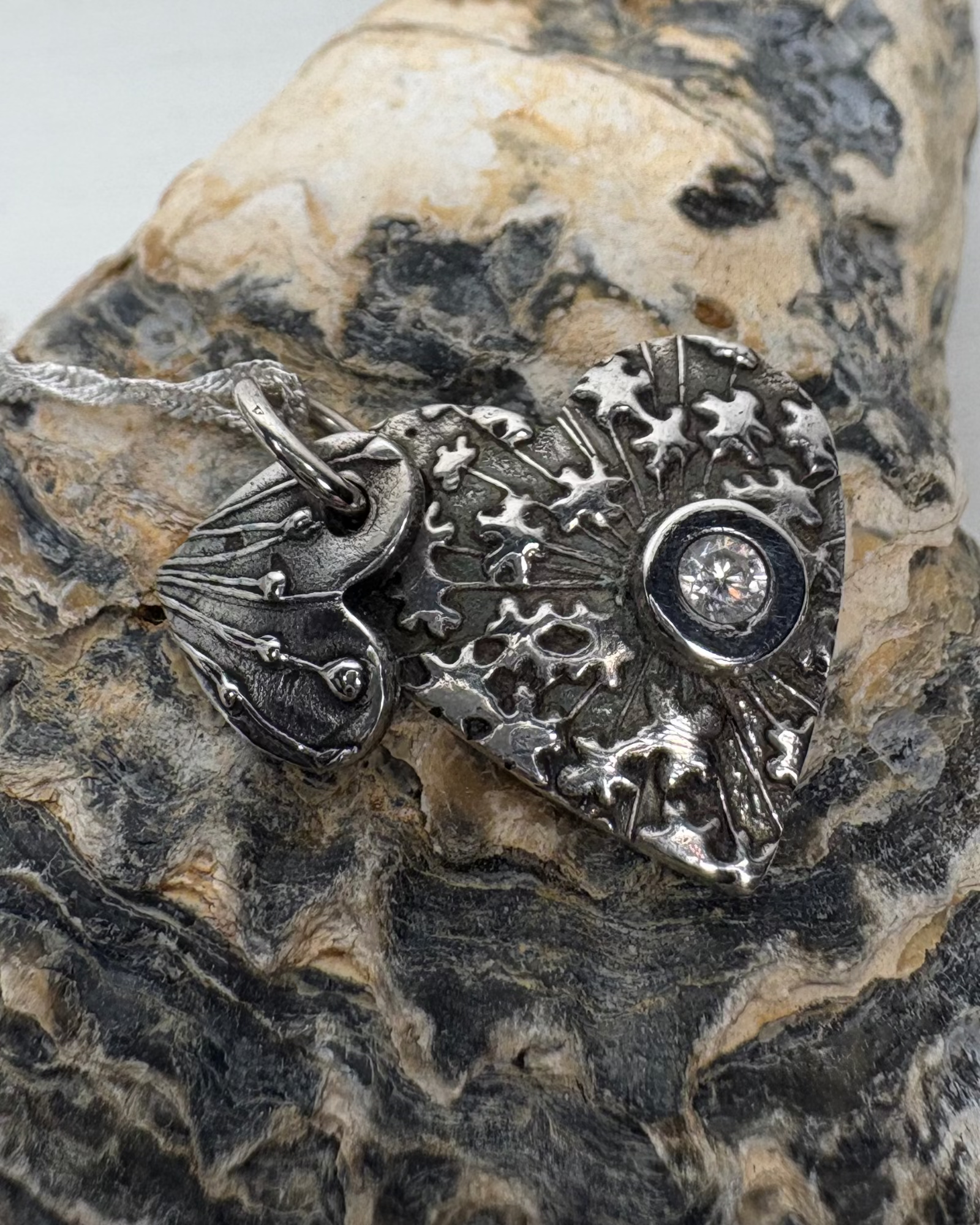 Silver necklace with 2 heart charms with seed head texture with a circular set clear zirconia pictured on a shell