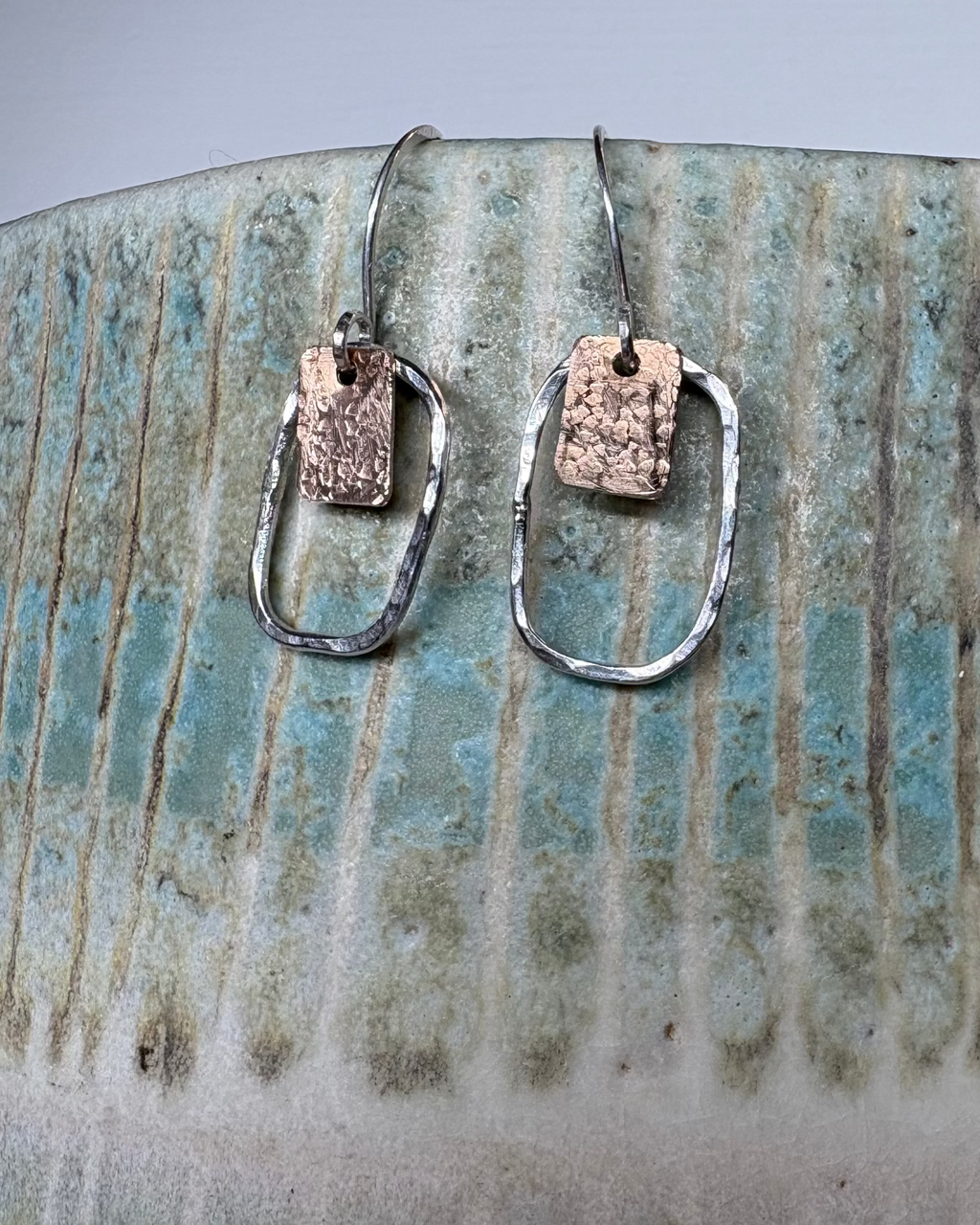 Pair of silver earrings with textured bronze squares on a ceramic background