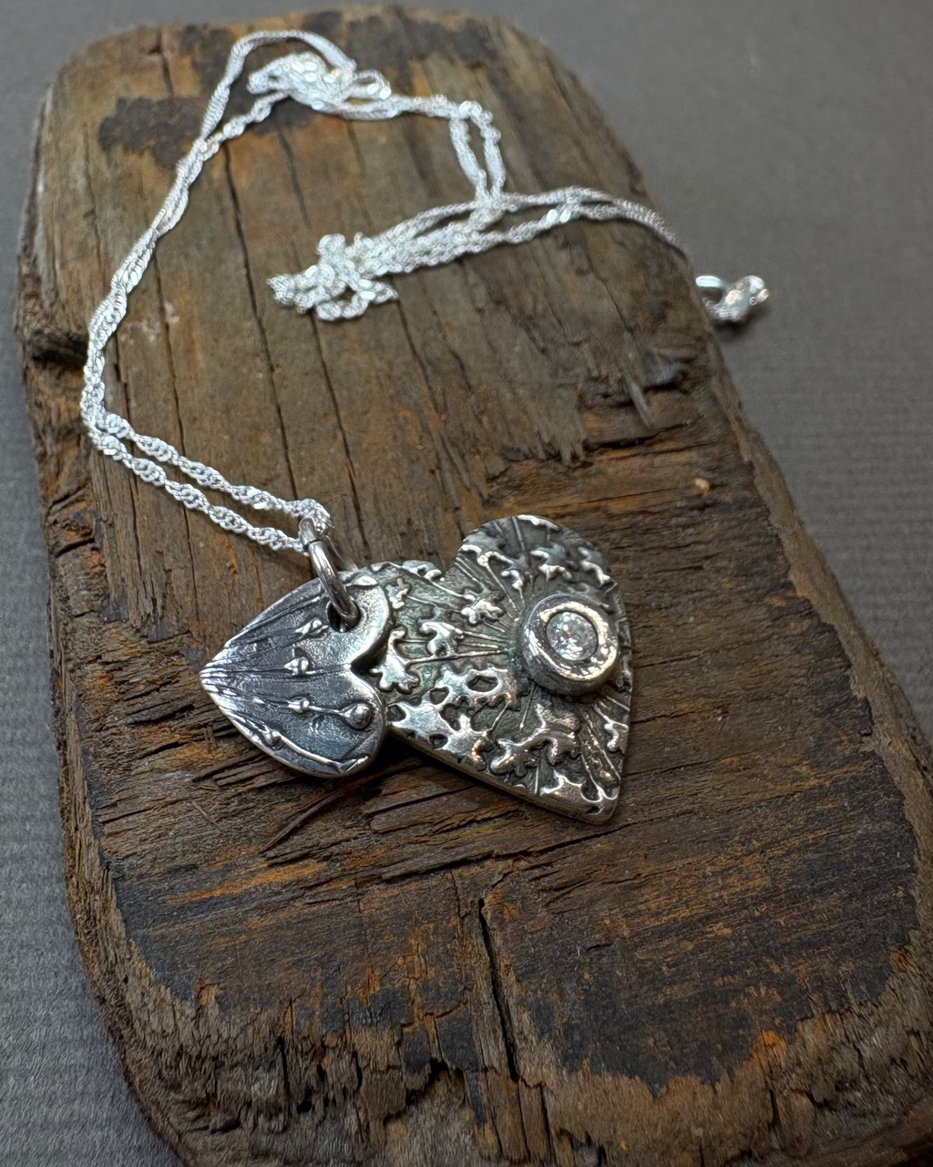 Silver double heart necklace with a silver chain on a driftwood block