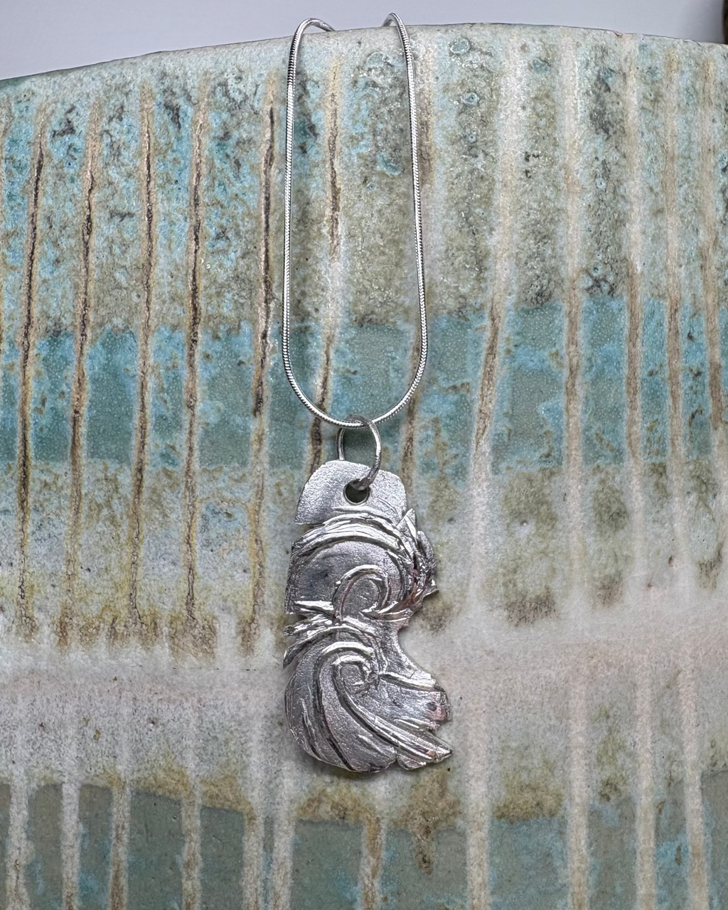 Silver surf pendant on a textured ceramic surface
