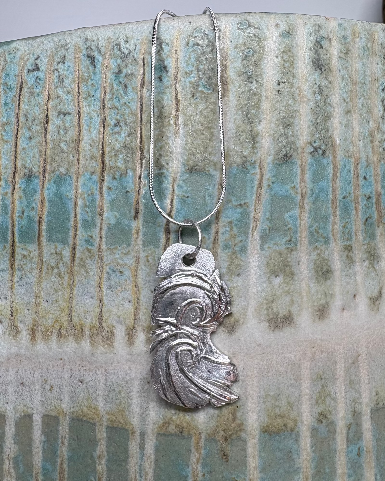 Silver surf pendant on a textured ceramic surface