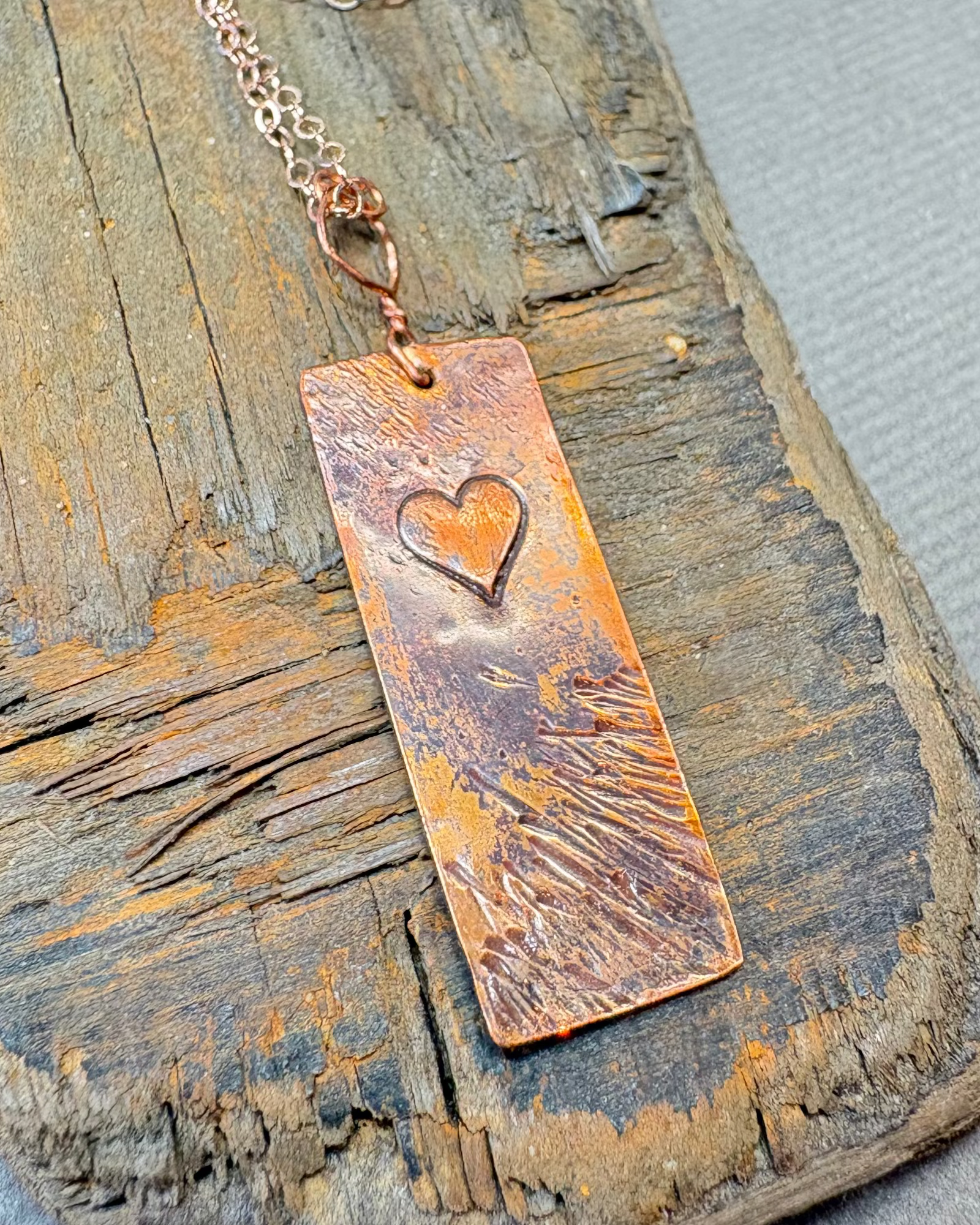 Copper textured and oxidised necklace with a heart stamp on a dirftwood surface