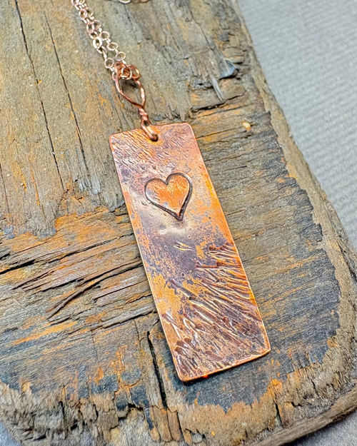 Copper textured and oxidised necklace with a heart stamp on a dirftwood surface