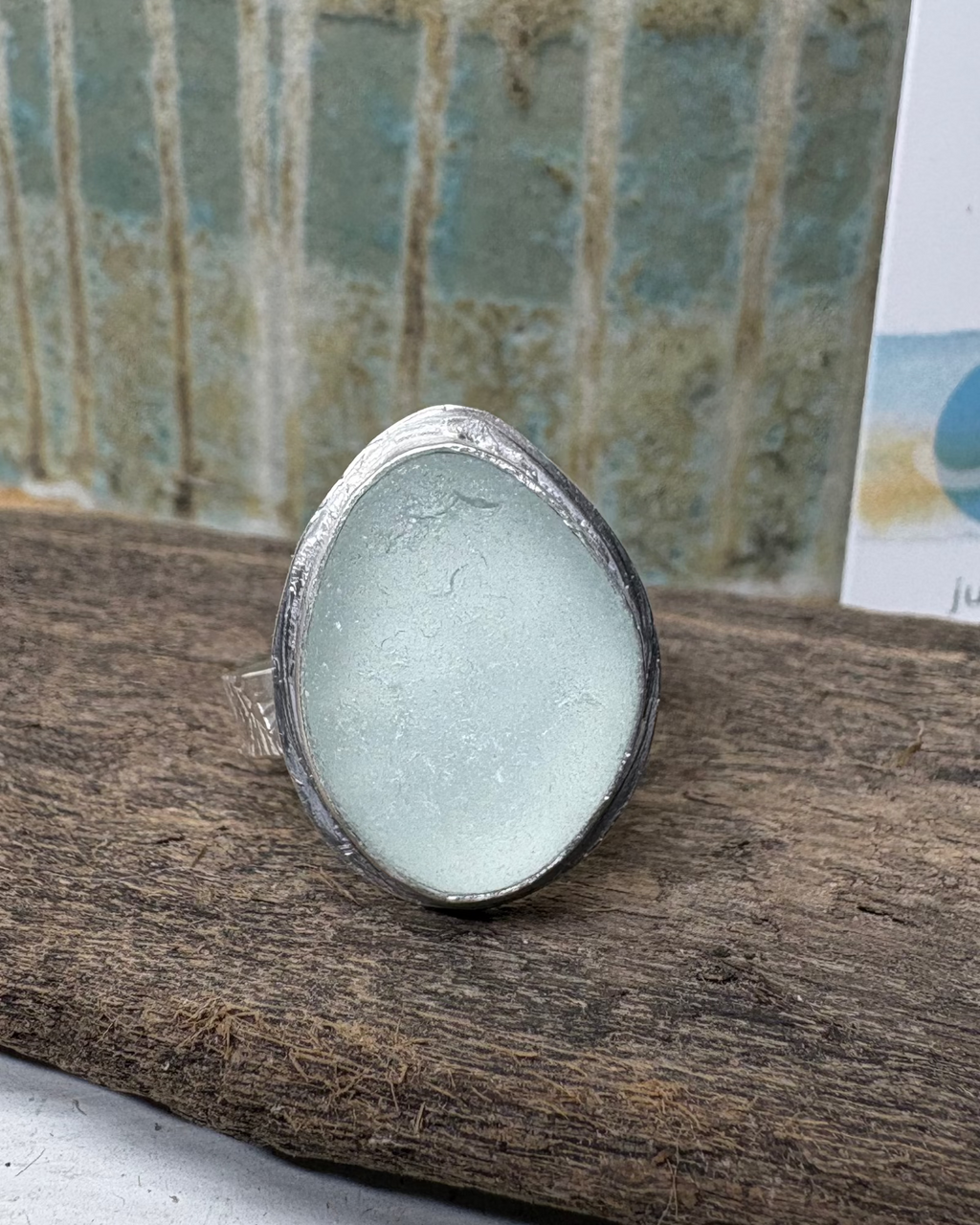 Silver halo set ring with a light aqua sea glass on a drift wood surface