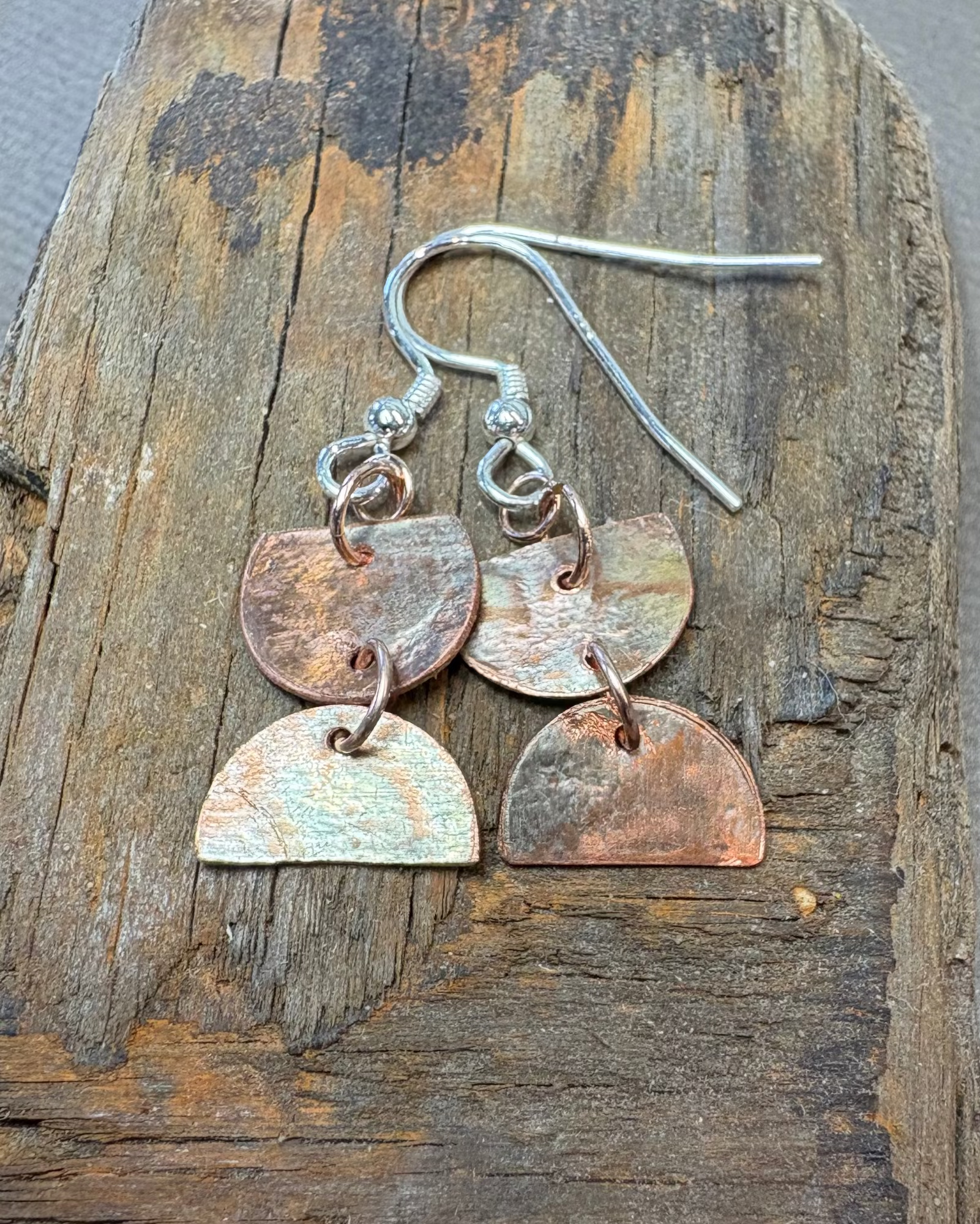 Pair of oxidised and textured copper and silver earrings on a driftwood surface