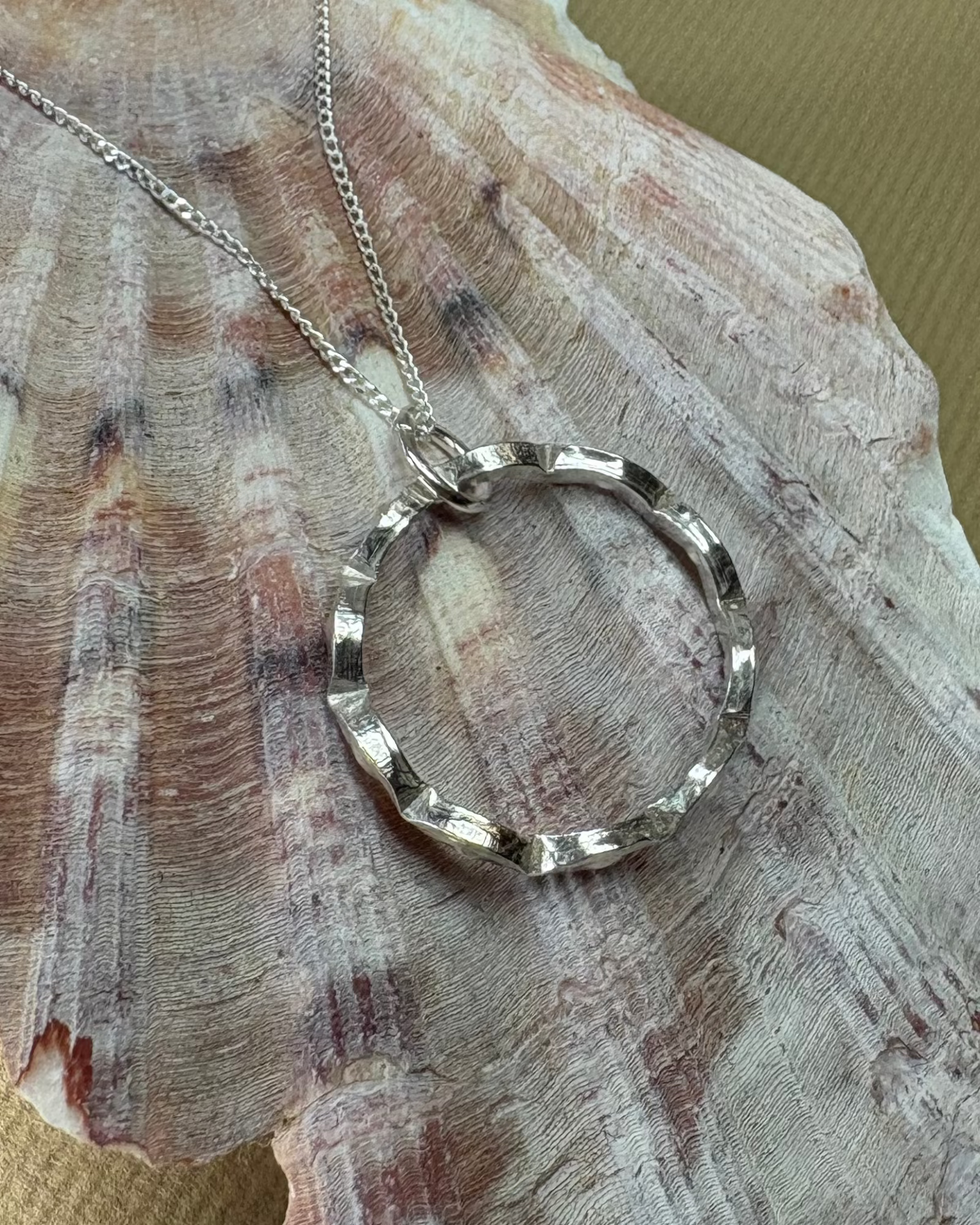 Silver necklace with a wavy silver circular pendant on a large shell 