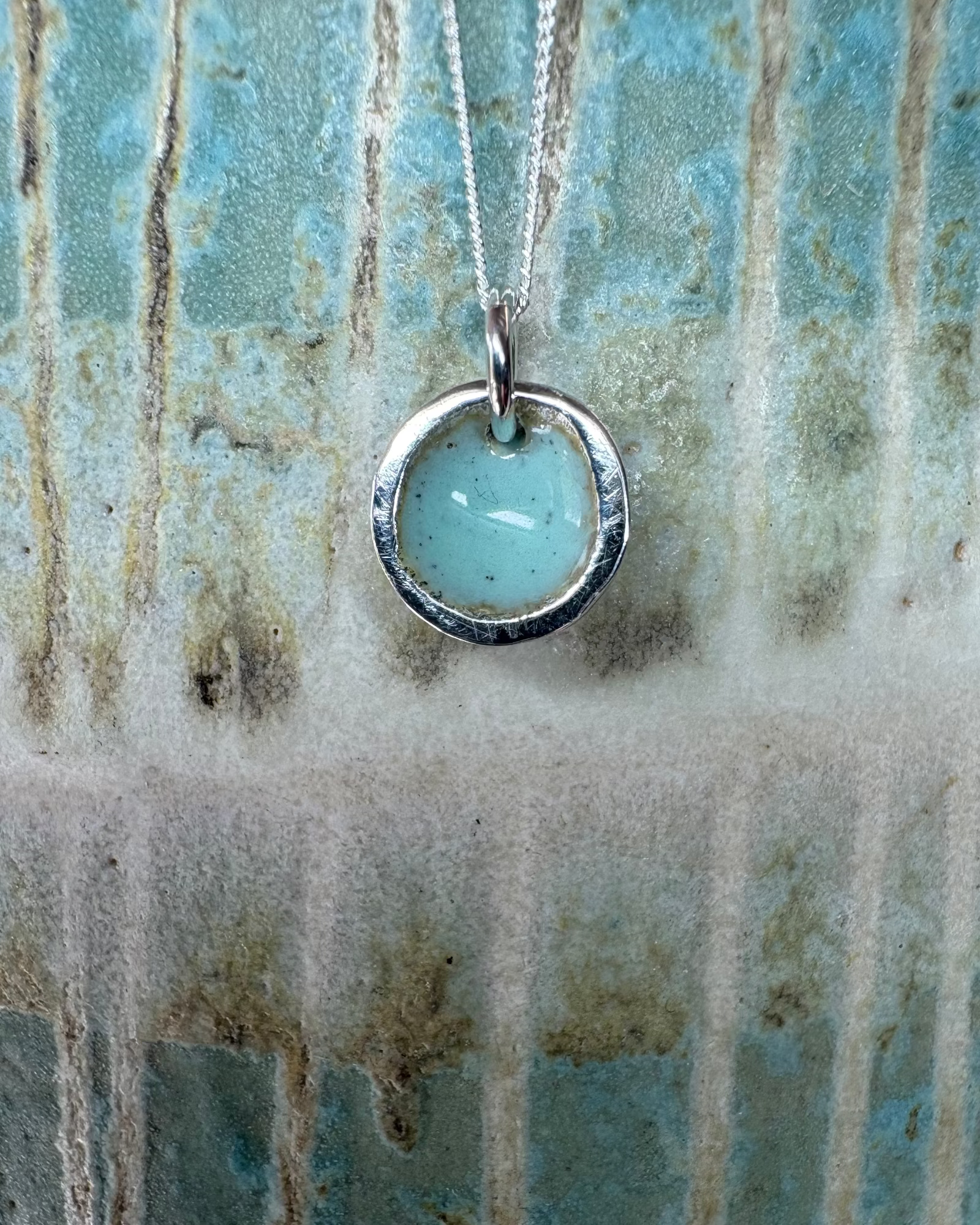 Silver necklace with a turquoise enamel on a textured background