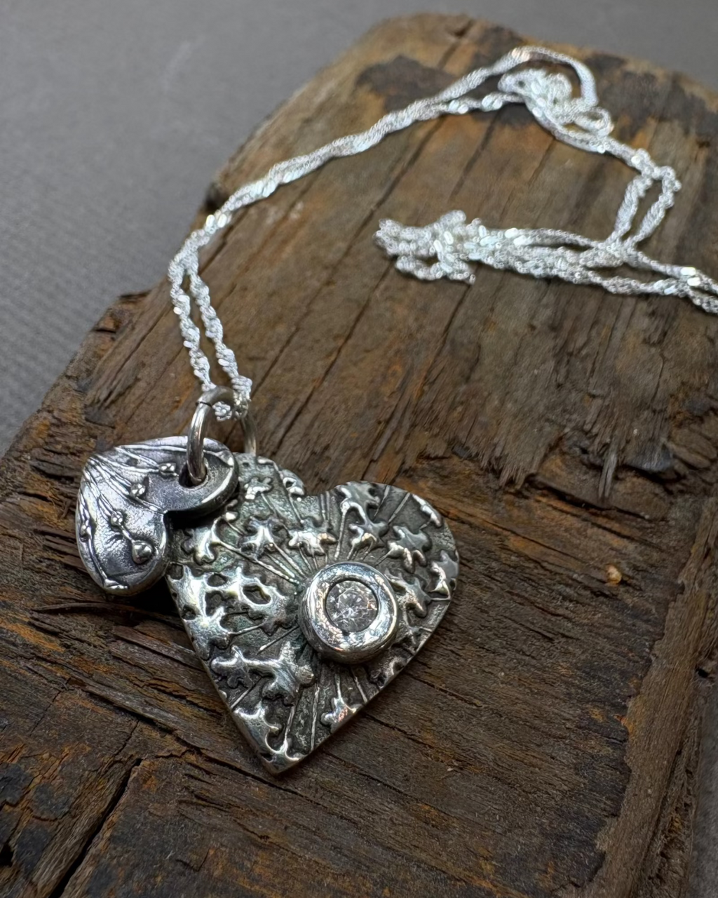 Silver patterned double heart pendant with clear cubic zirconia on a silver chain on a driftwood surface