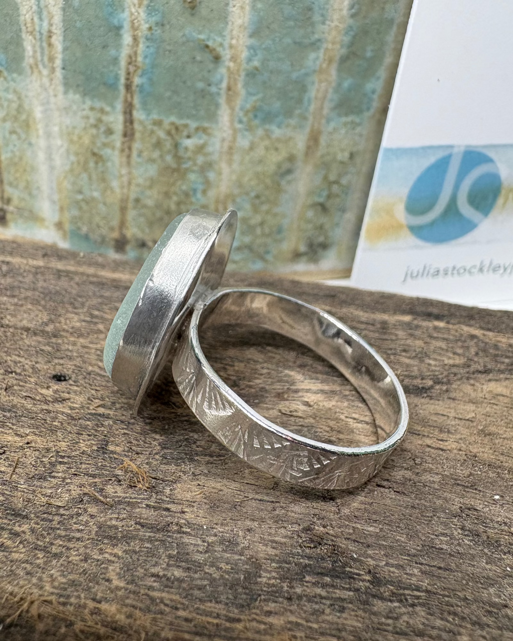 Silver ring with embossed shell design on band on a driftwood surface