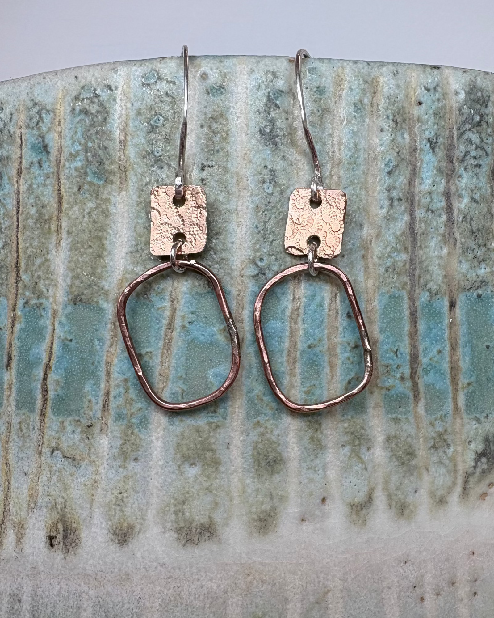 Bronze hoop earrings with textured rectangles on a textured ceramic background