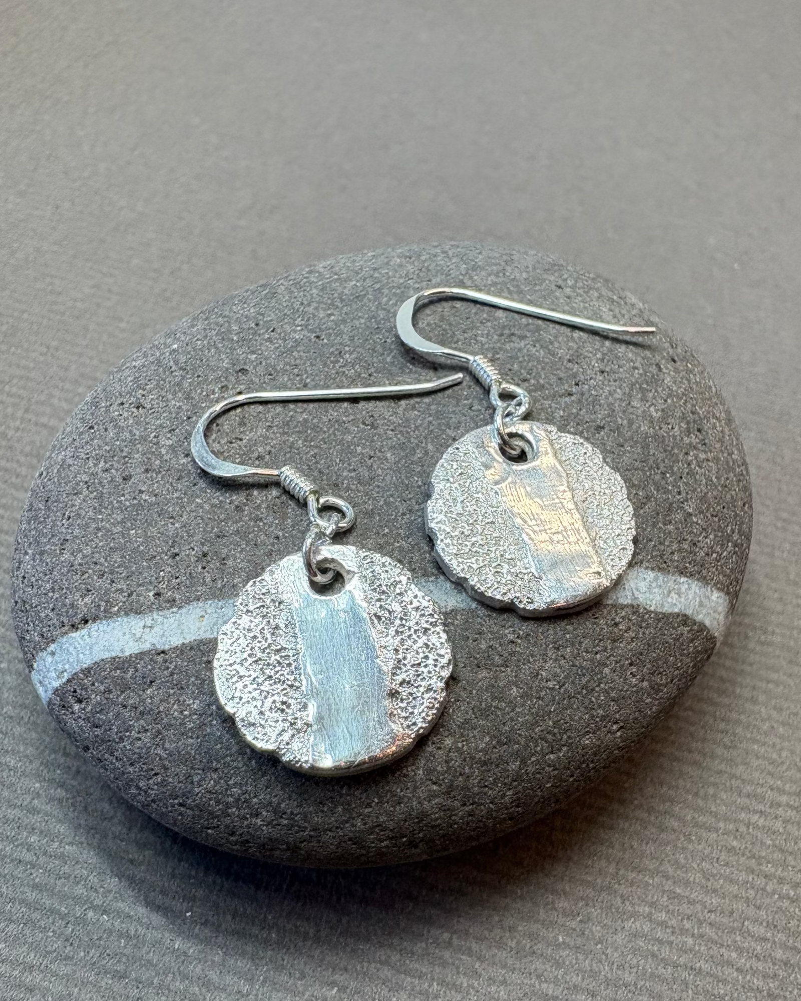 Round silver smooth and texture earrings on a pebble