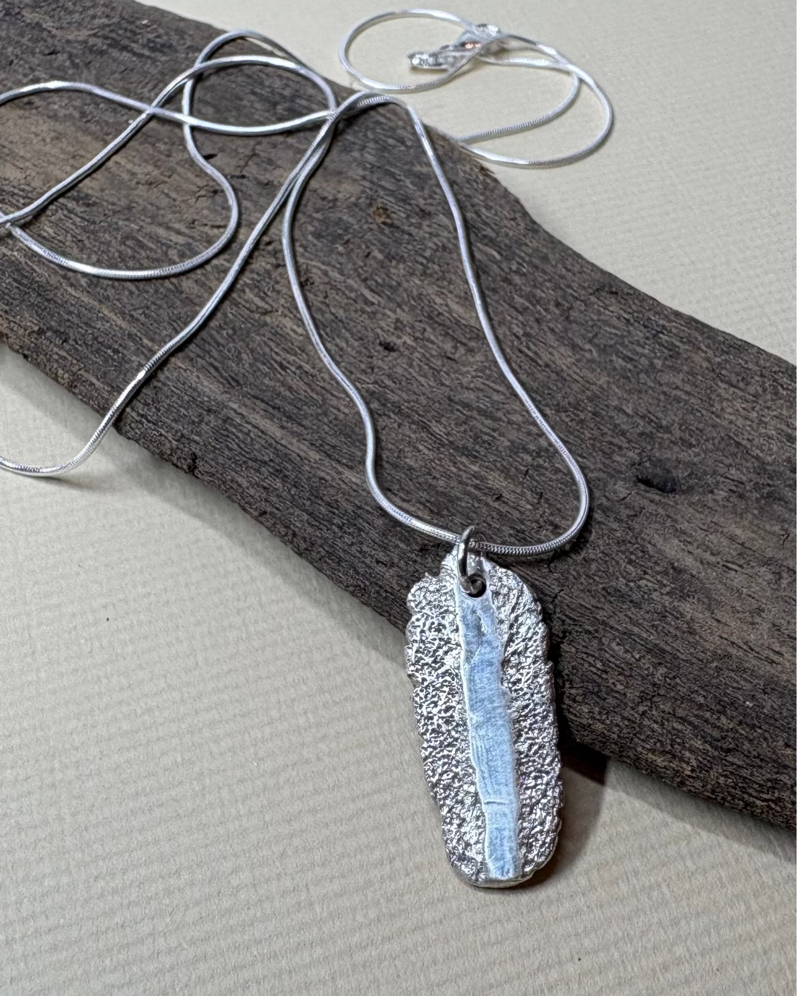 Silver rough and smooth texture oval necklace with silver chain on driftwood background