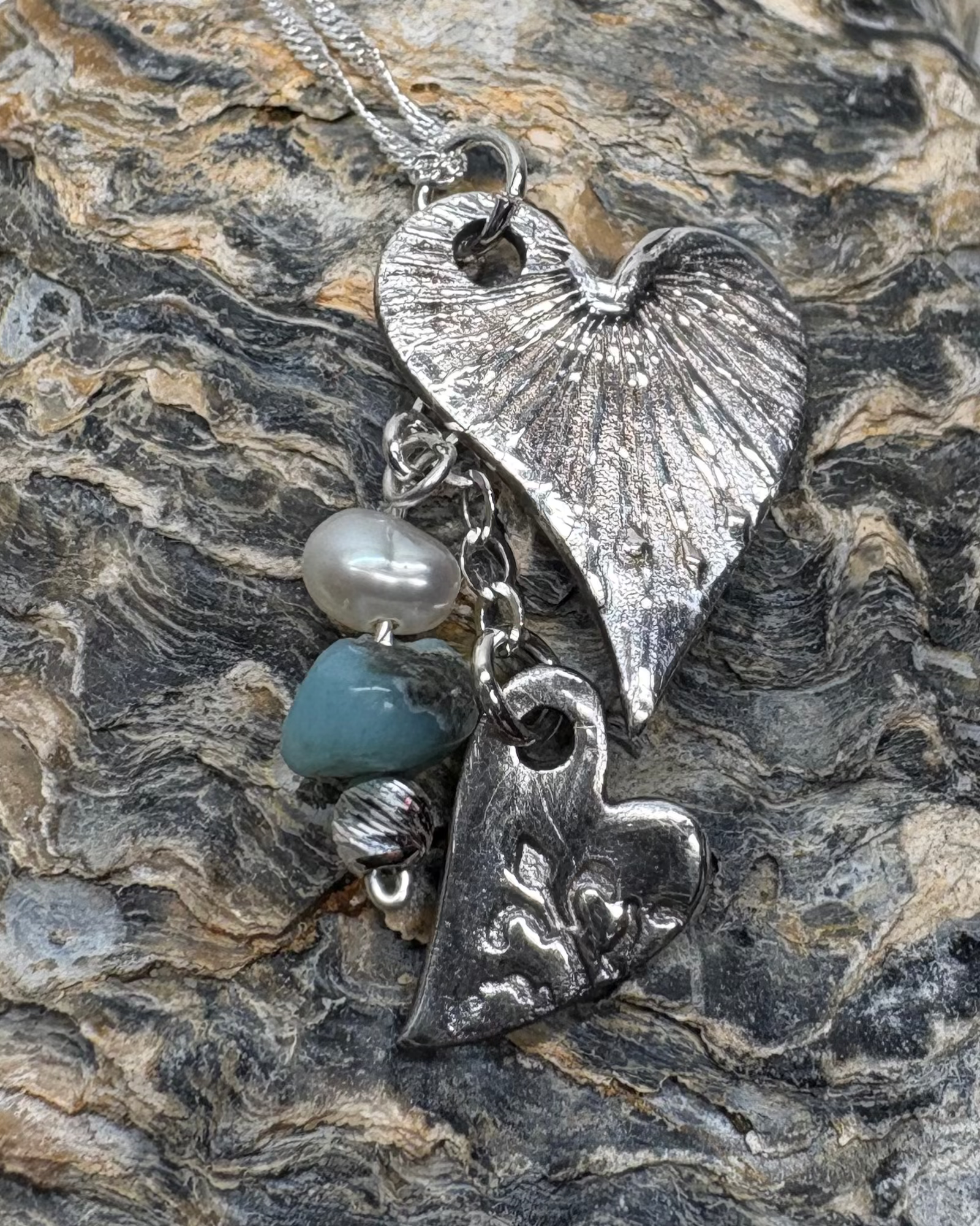 Silver hearts necklace with apetite stone and pearl on a textured shell surface