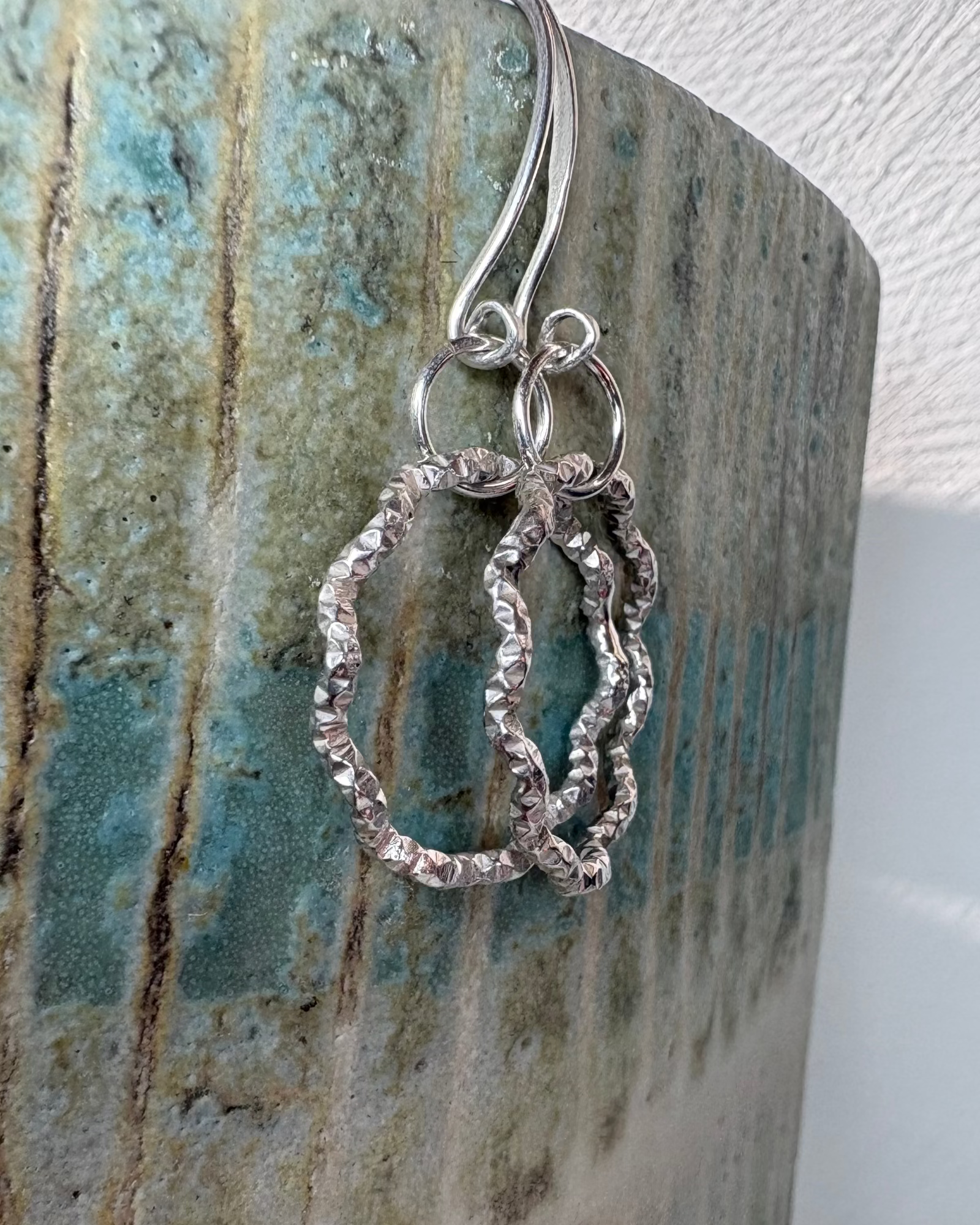 Silver wavy hoop earrings hanging on a ceramic surface