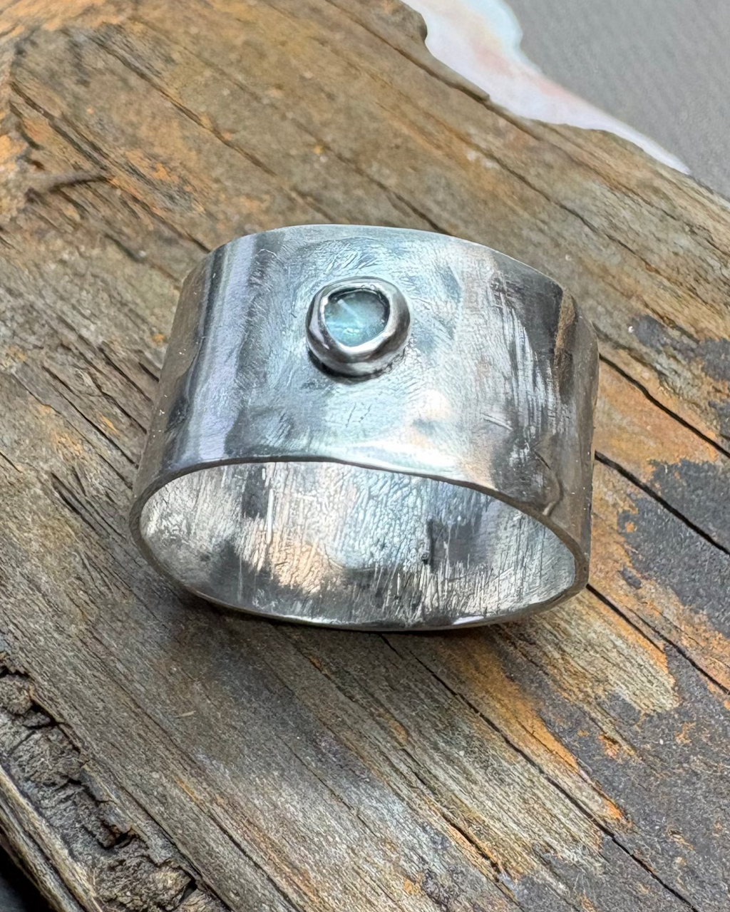 Hammered silver ring with bezel set blue topaz stone pictured on driftwood