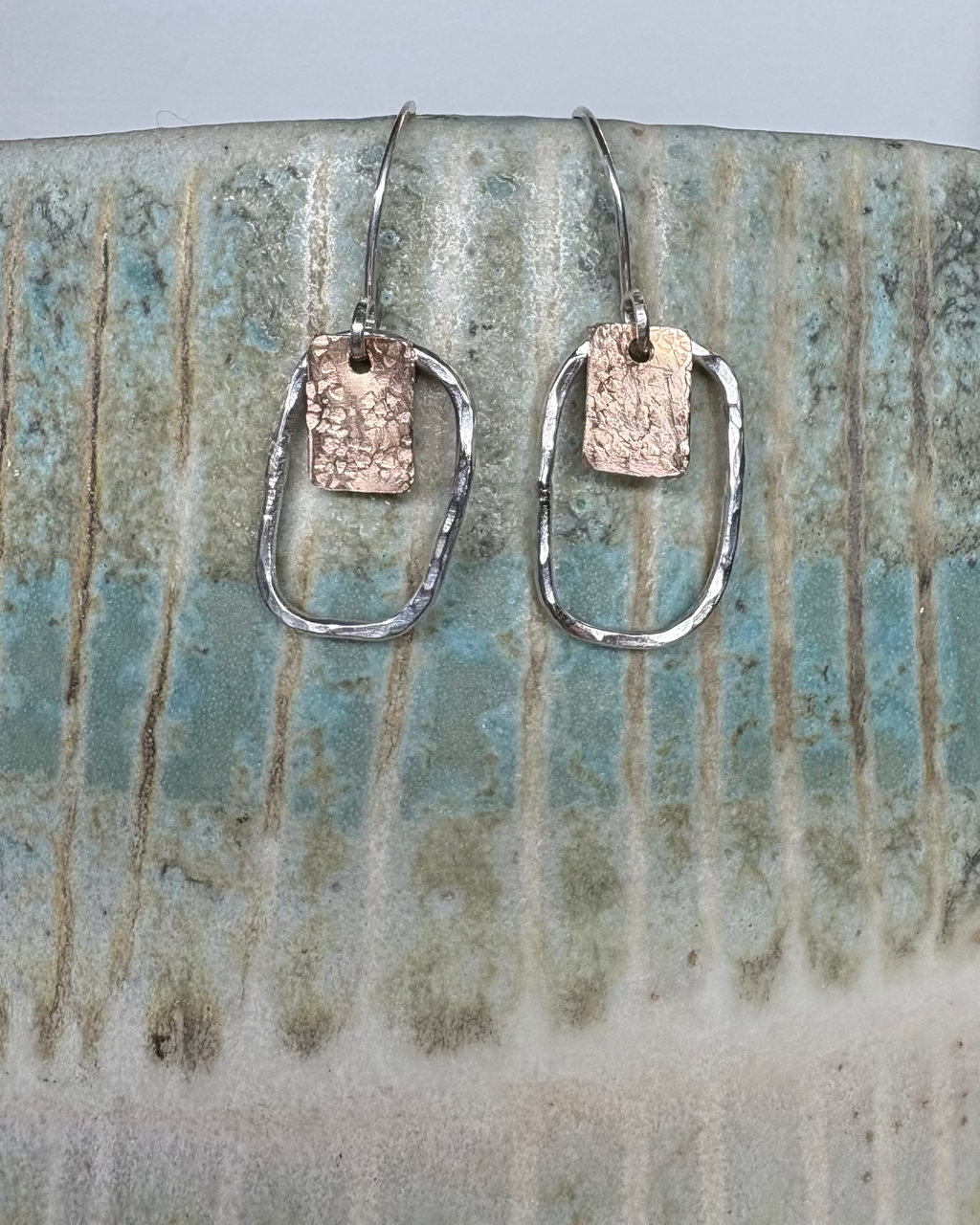 Pair of silver earrings and bronze earrings on a ceramic vase