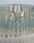 Pair of silver earrings and bronze earrings on a ceramic vase