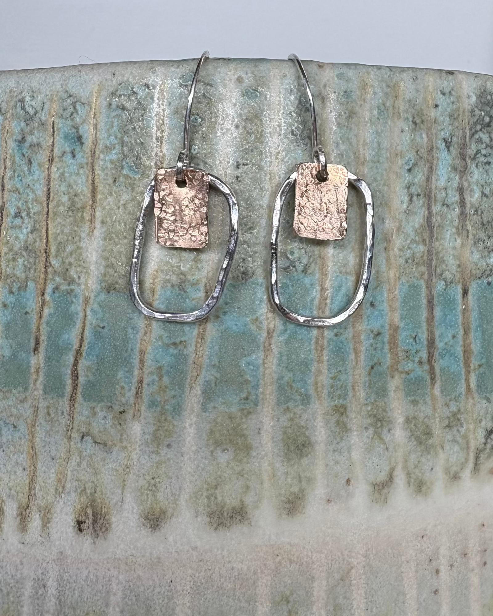 Pair of silver earrings and bronze earrings on a ceramic vase