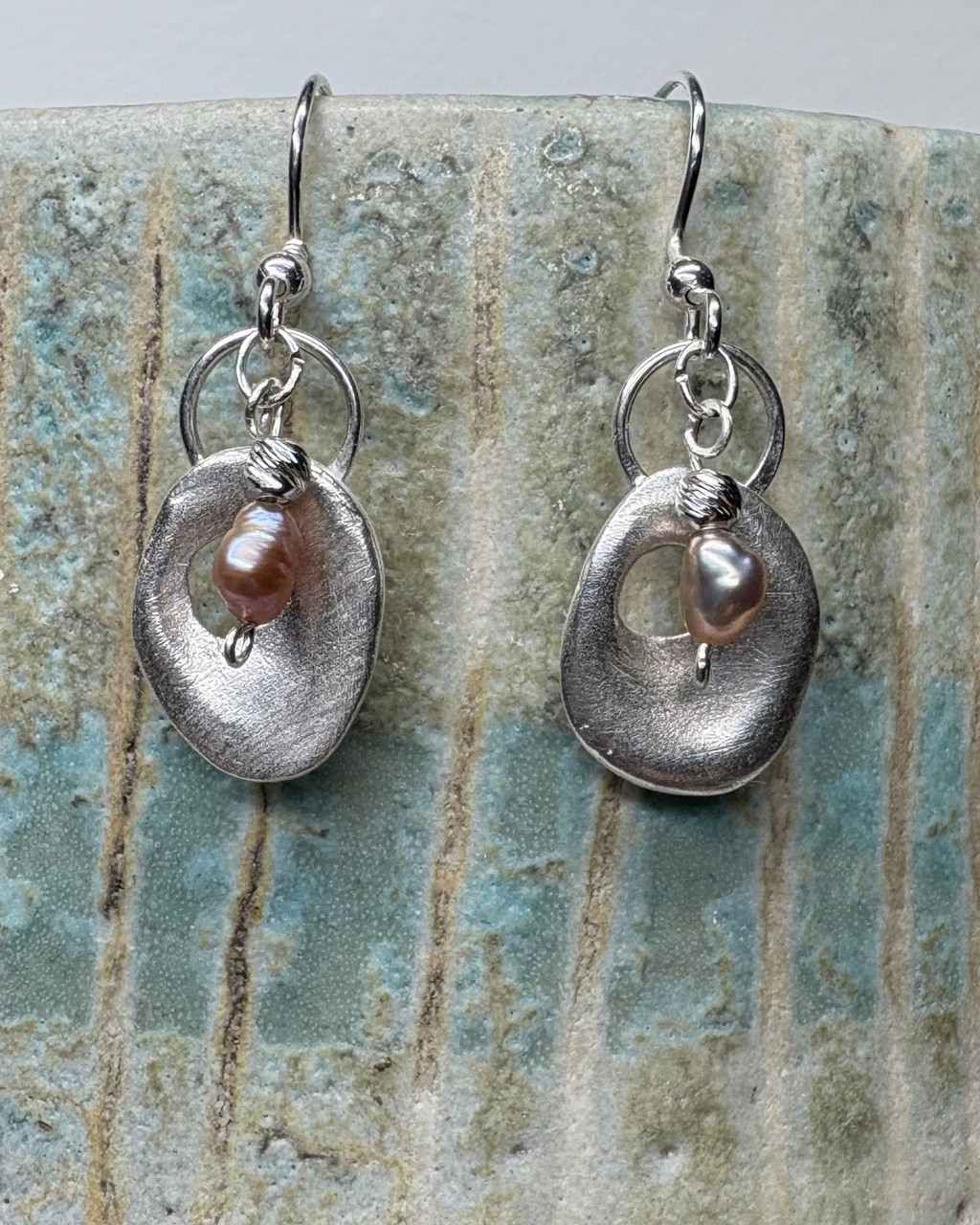 Pair of silver earrings with pink pearls on a textured ceramic surface