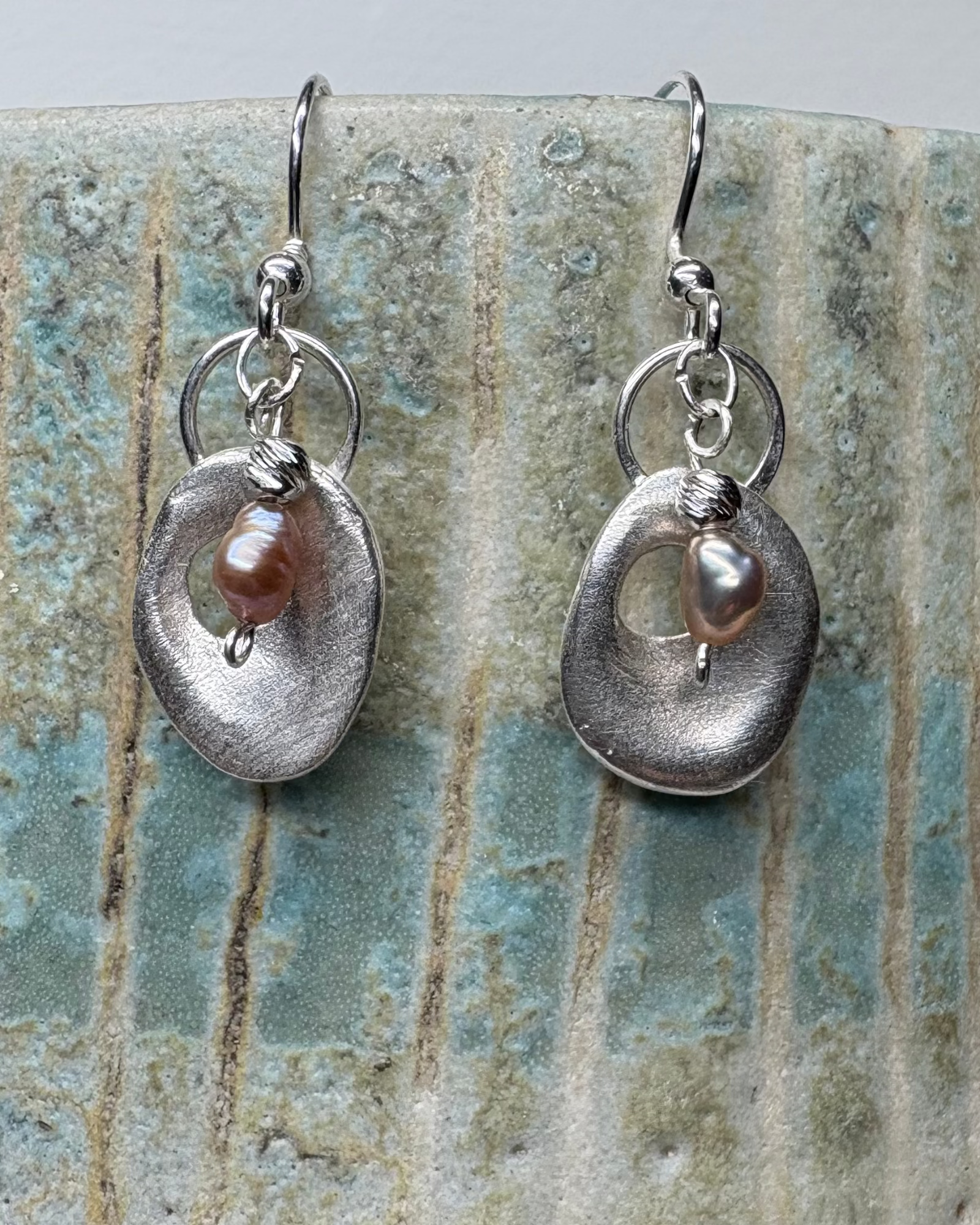 Pair of silver earrings with pink pearls on a textured ceramic surface