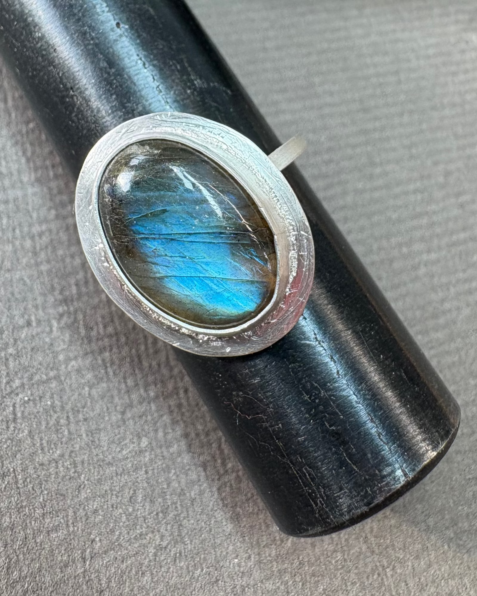 Silver ring with a bezel set labradorite gemstone on a grey surface
