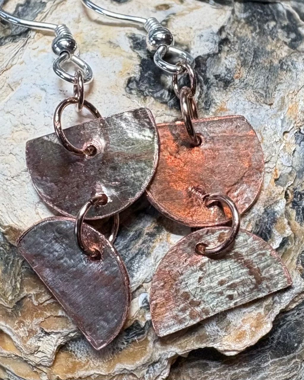 Copper half circles meeting with joining rings oxidised and lace pressed surface silver ear wires on shell background