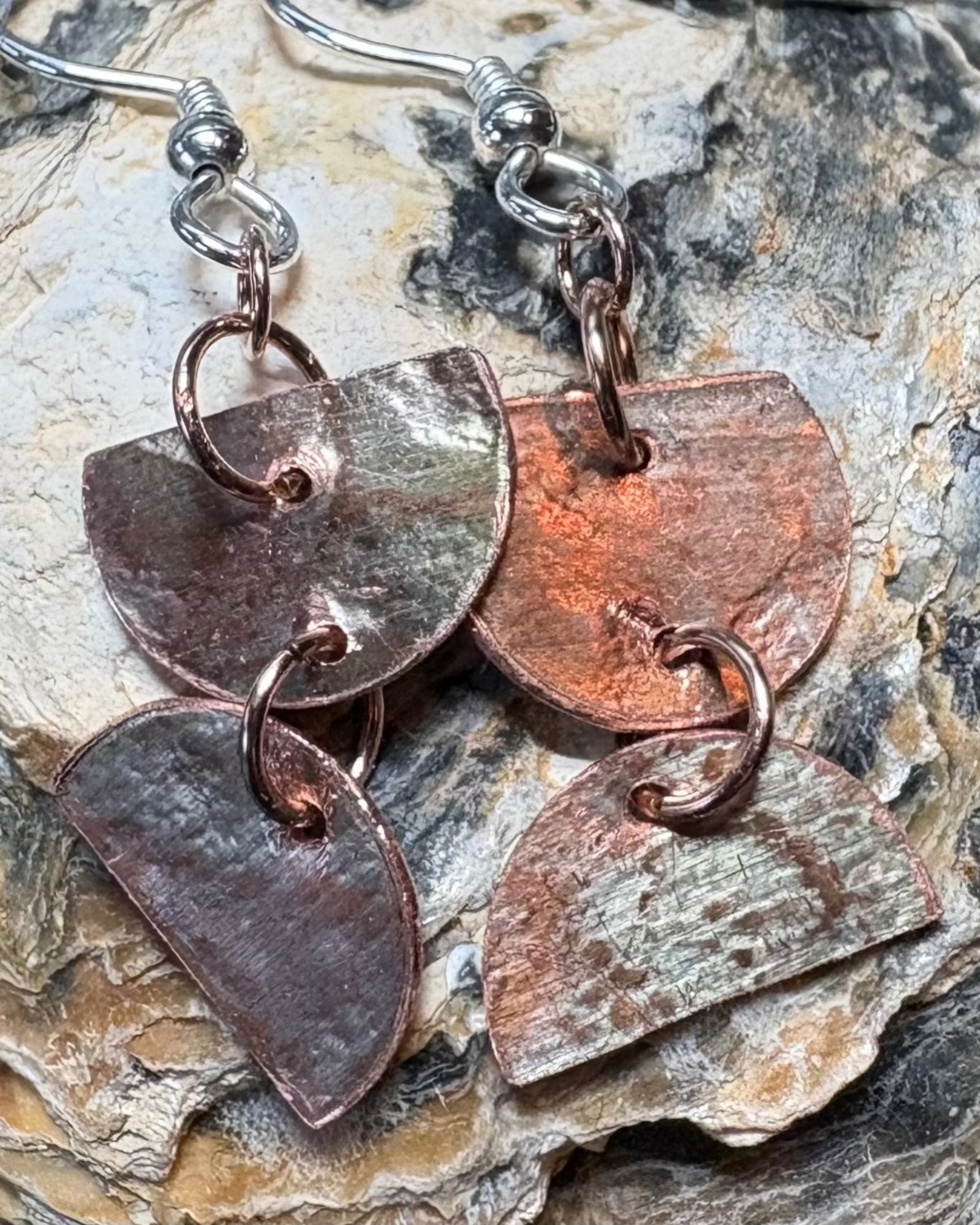 Copper half circles meeting with joining rings oxidised and lace pressed surface silver ear wires on shell background