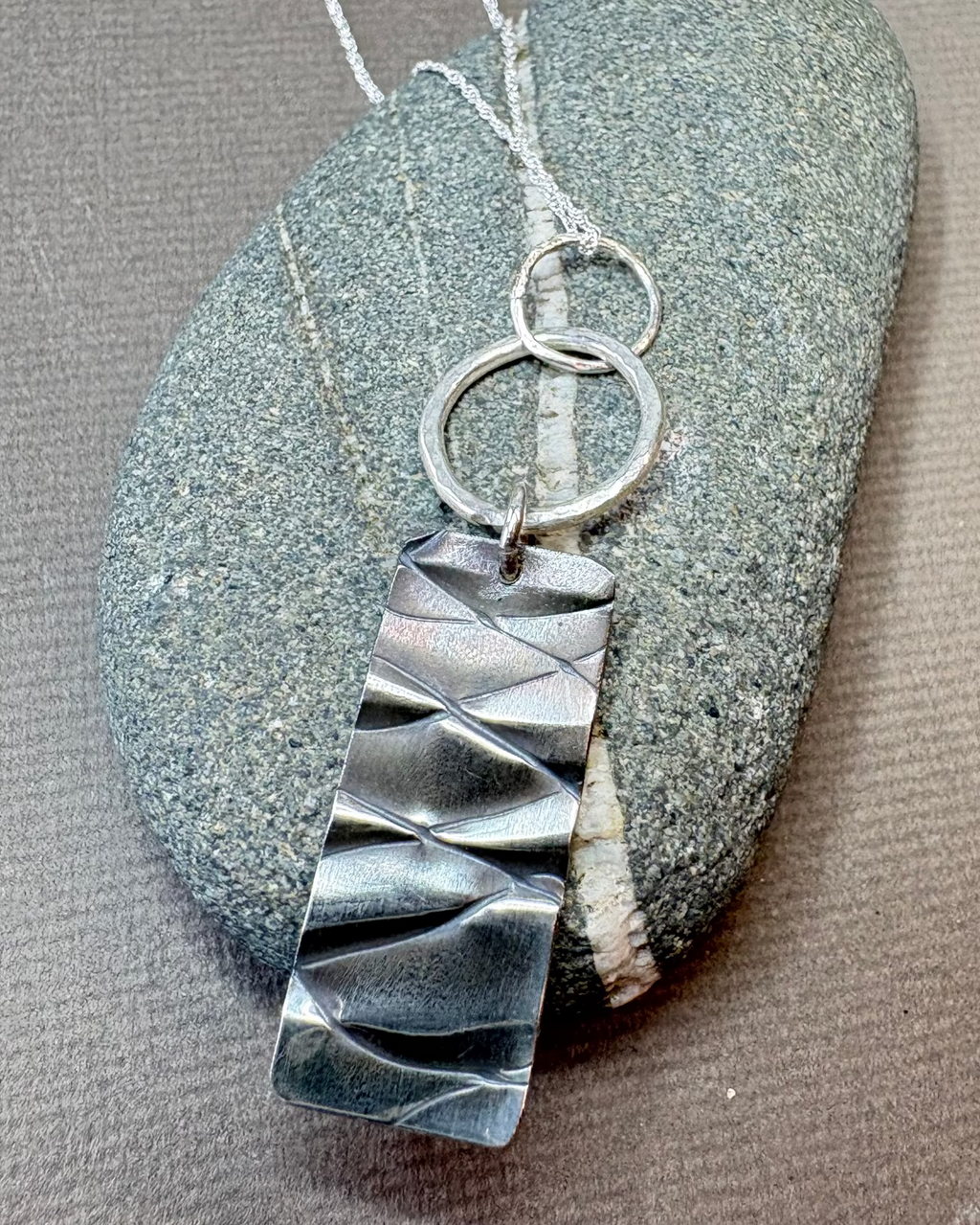 Silver hoop and texture pendant necklace on a pebble surface