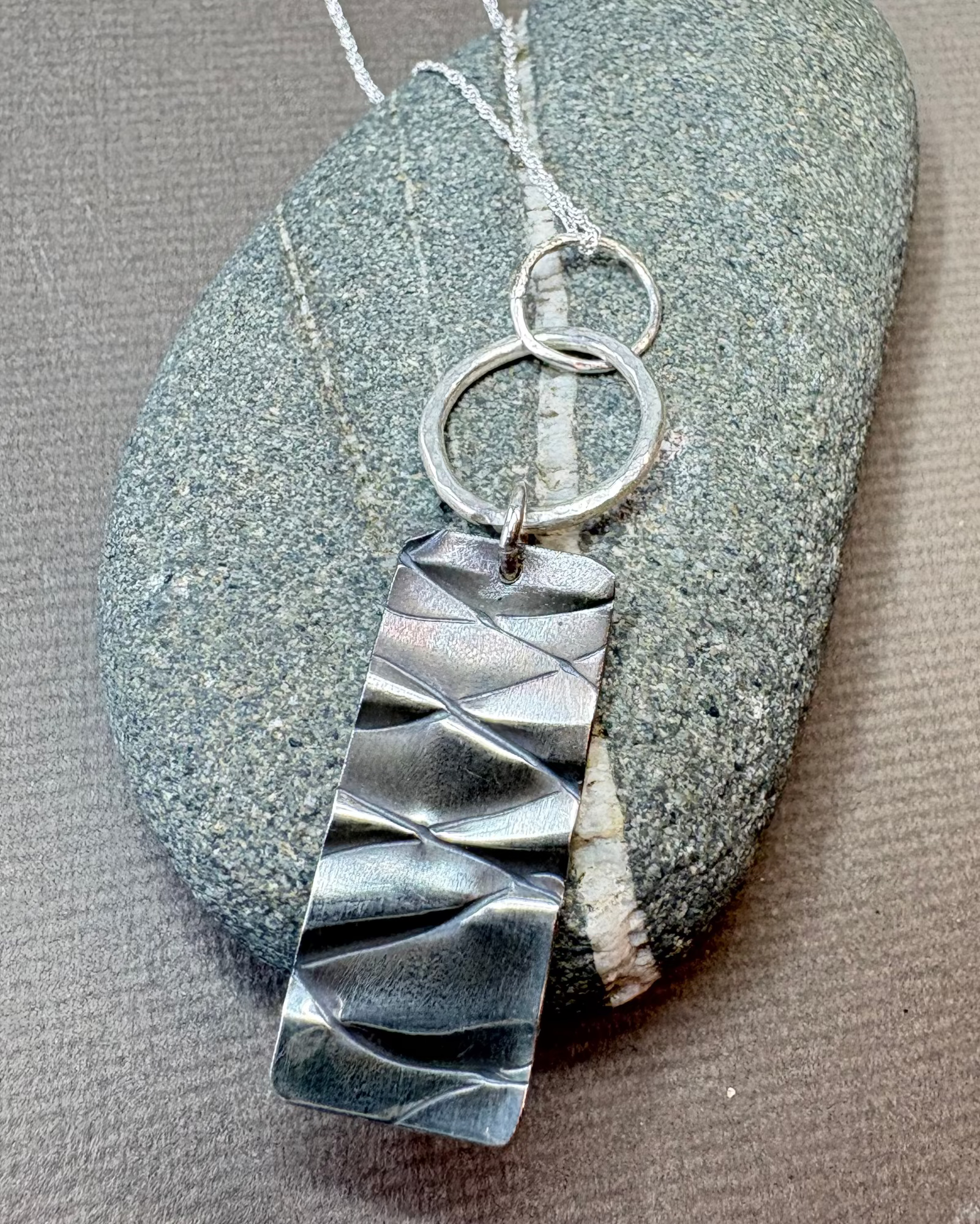 Silver hoop and texture pendant necklace on a pebble surface
