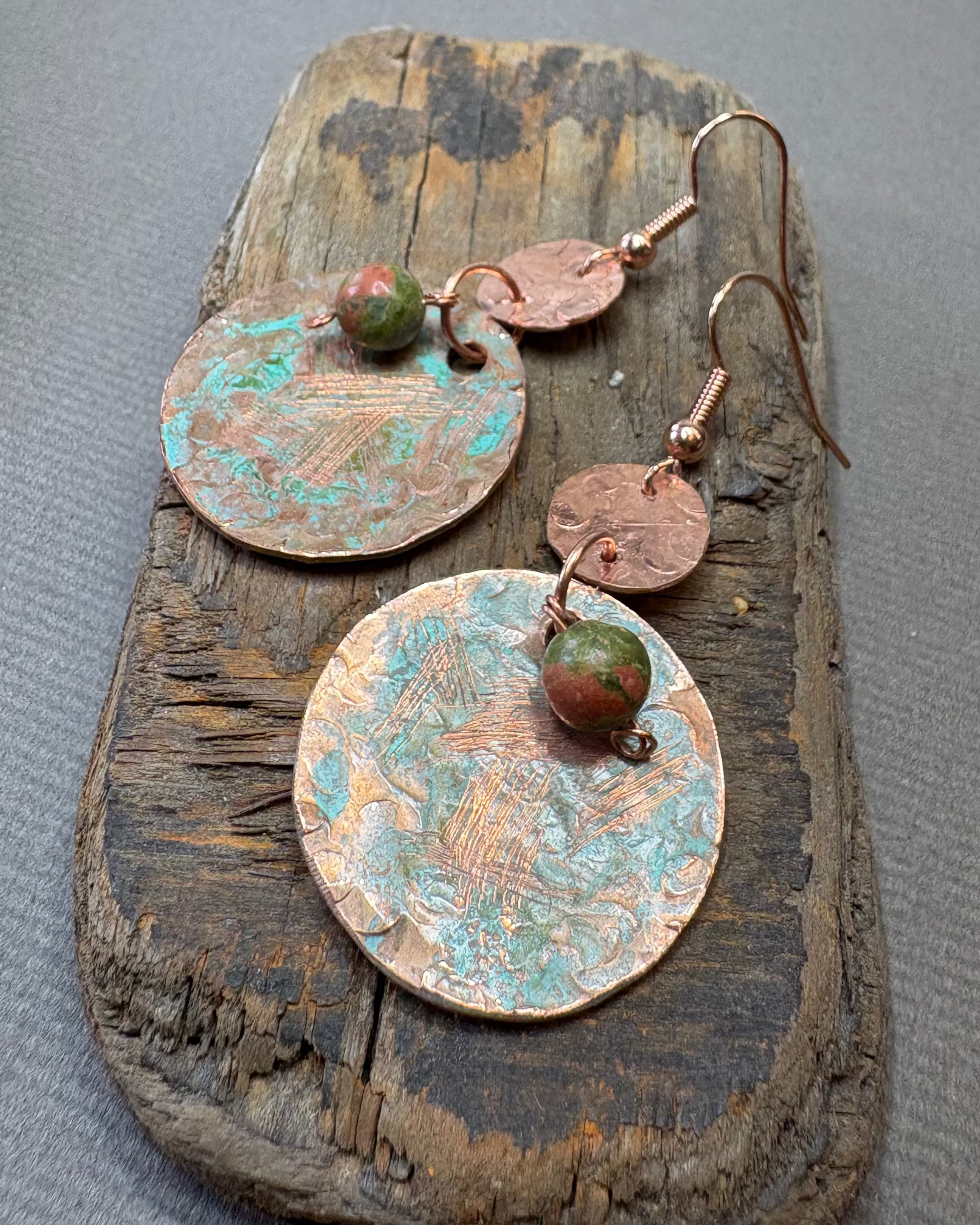 Pair of copper circle earrings with green patina and unakite beads on a driftwood surface