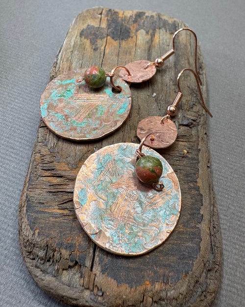 Pair of copper circle earrings with green patina and unakite beads on a driftwood surface