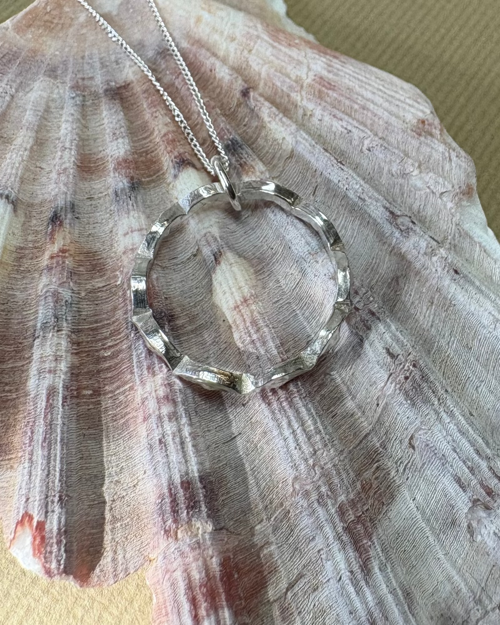 Silver necklace with a circular pendant on a large shell against a gold background