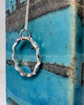 Silver wavy circle pendant necklace on a textured blue surface