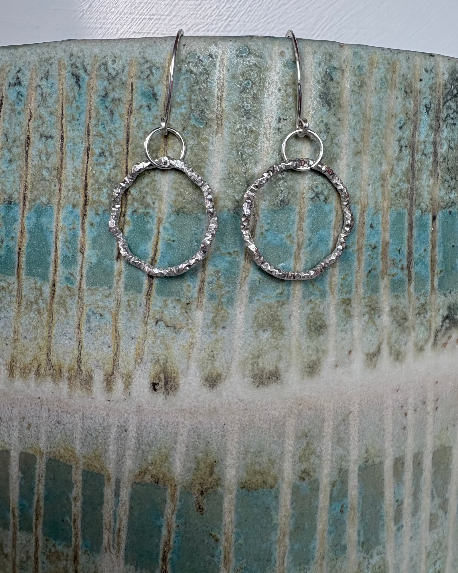Silver wavy hoop earrings on a ceramic surface