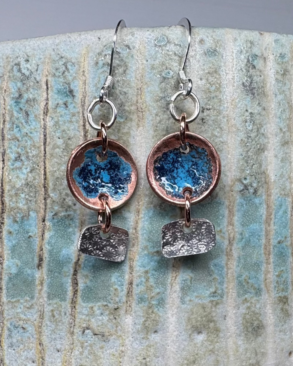 Enamelled copper and textured silver earrings on a stoneware background