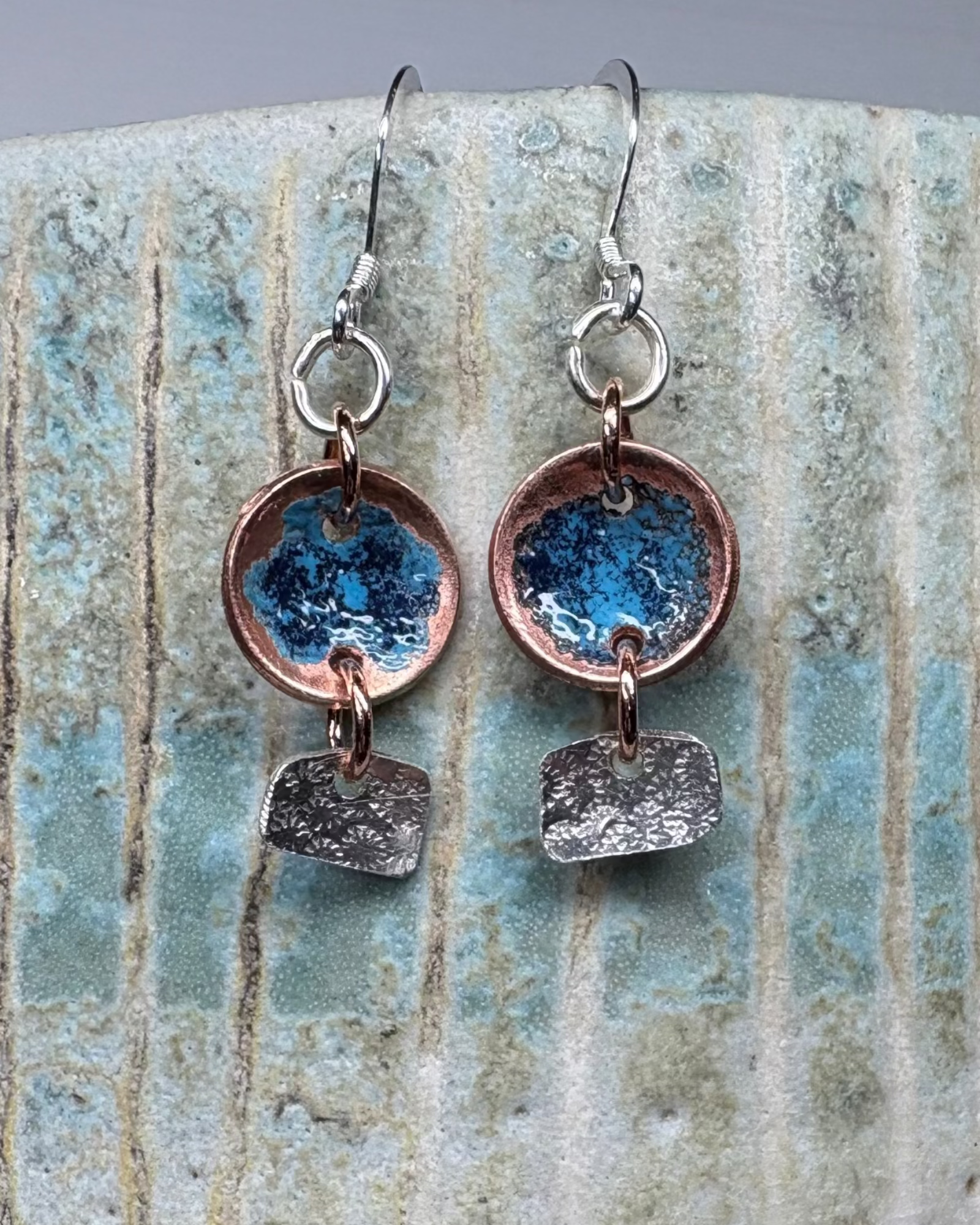 Enamelled copper and textured silver earrings on a stoneware background