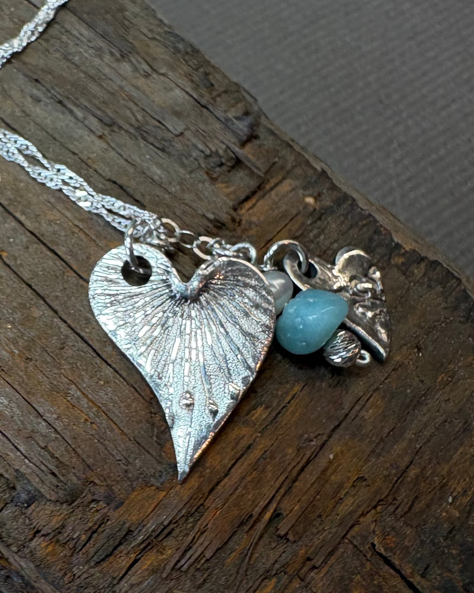 Silver hearts charms necklace with silver chain and turquoise apatite bead on driftwood surface